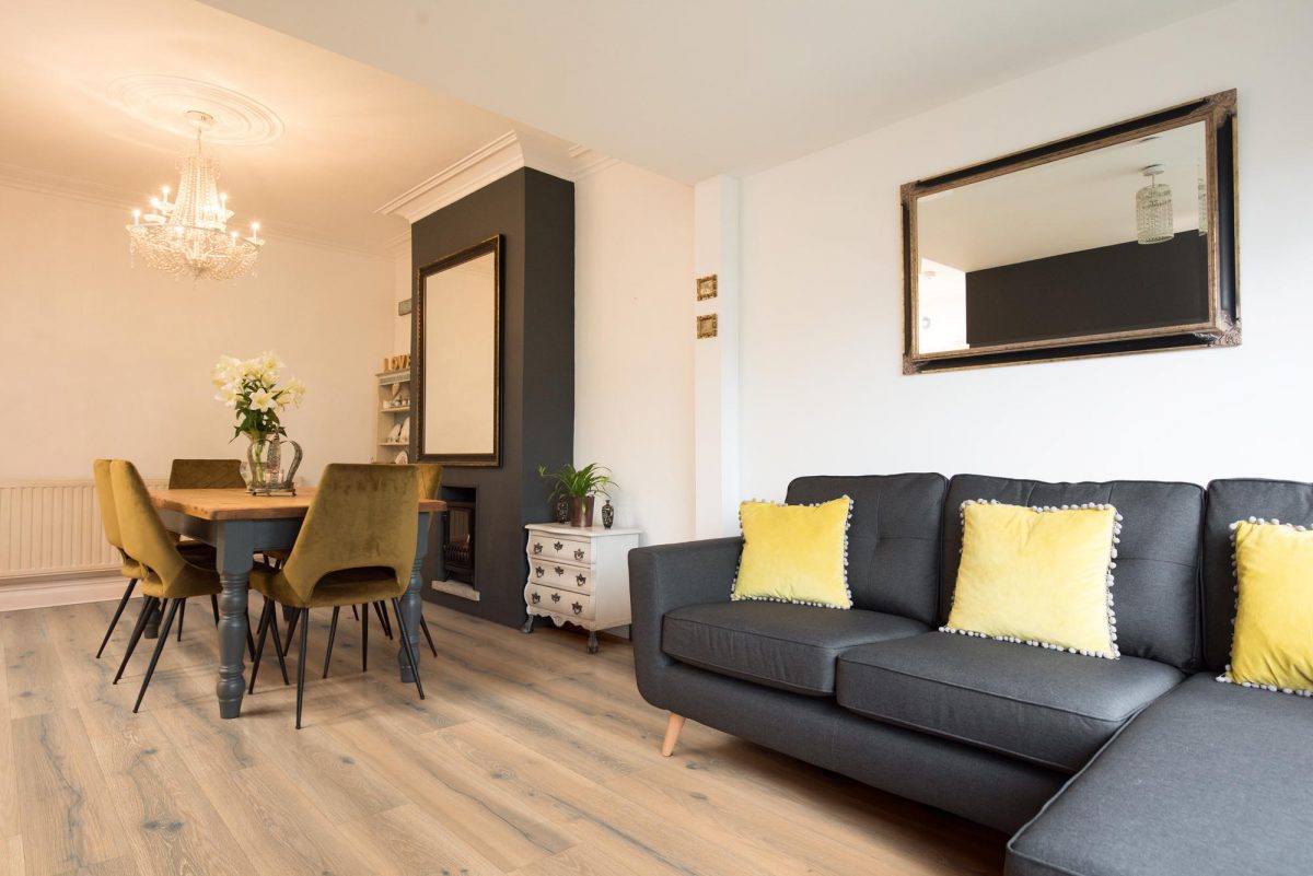 A dining sitting room with reclaimed pine farmhouse style dining table with painted legs and modern mustard coloured velvet dining chairs with grey sofa